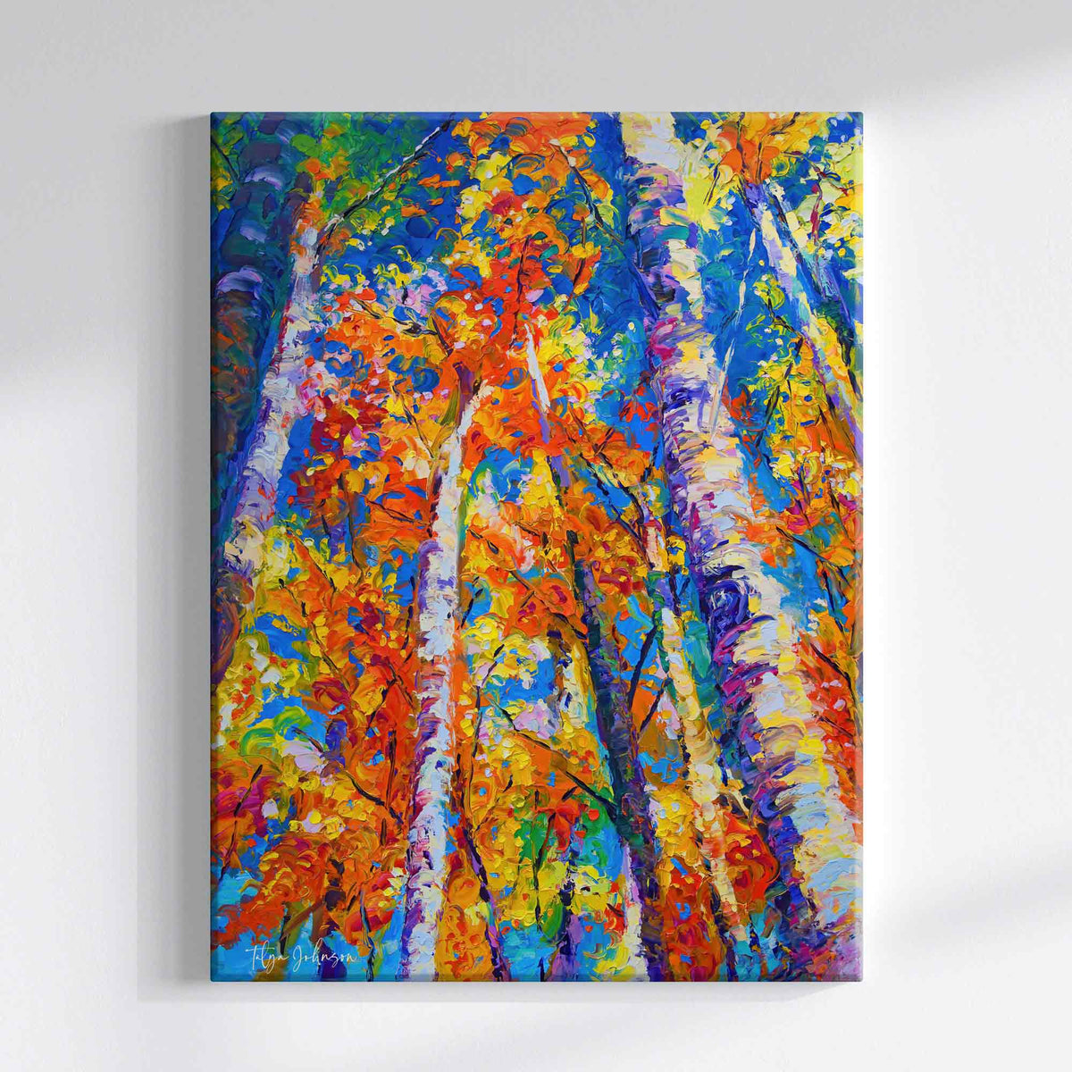 Birch tree art: a vertical canvas painting of birch trees in autumn by Oregon modern impressionist artist Talya Johnson, featuring vibrant brushstrokes of orange, yellow foliage against a blue sky and colorful trunks, displayed on a light gray wall. 