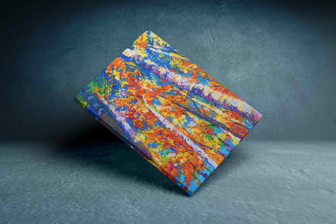 A square canvas painting featuring a vibrant, abstract forest scene with colorful autumn foliage in orange, yellow, red, and blue, displayed at an angle on a dark textured studio surface.