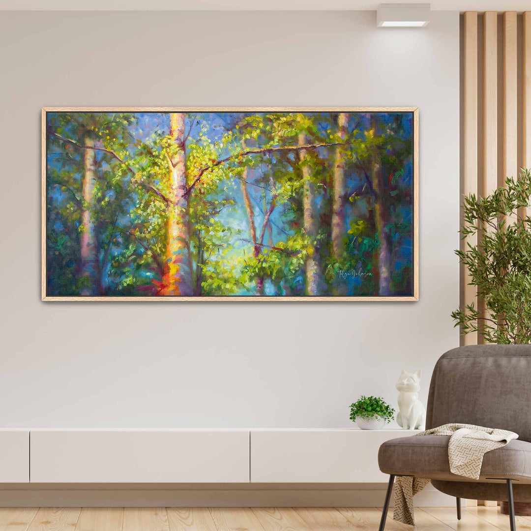 Oak framed canvas print of a forest scene painting on a wall above a sofa.