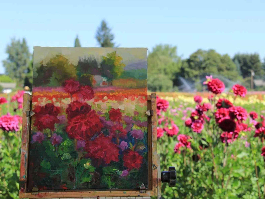 Painting in progress on easel of bright red purple dahlias in a sunlit dahlia farm. Painting by Talya Johnson