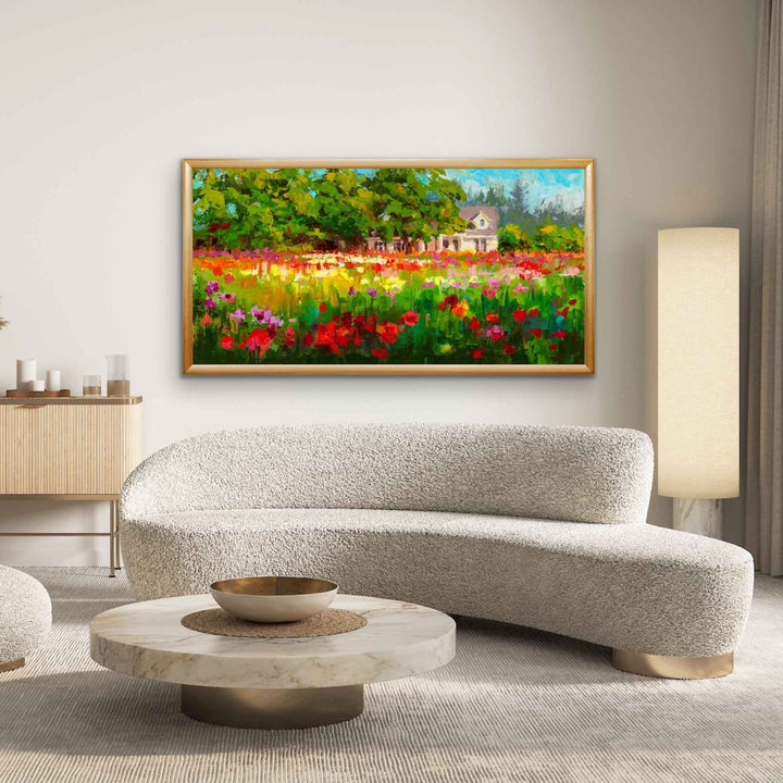 Impressionist large canvas art print of a white farmhouse and trees behind a field of colorful dahlias in the afternoon light. The artwork is has a light gold frame and hangs in a modern minimalist living room with neutral colors.