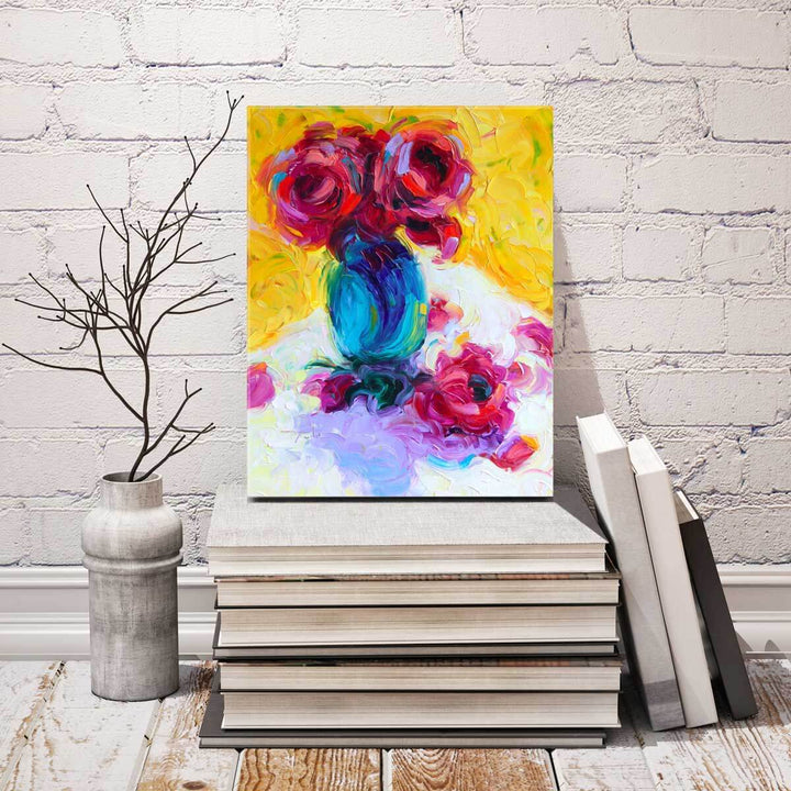 An original modern still life oil painting in the impressionism style with a turquoise vase white tablecloth, yellow background and abstract magenta red roses. Painting rests on a pile of books leaning against a white brick  wall.